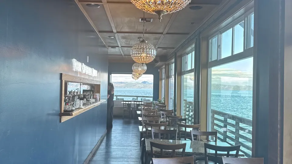 Pilot-boat seating: a row of tables along the windows, with the river outside and the kitchen's service window on the blue wall