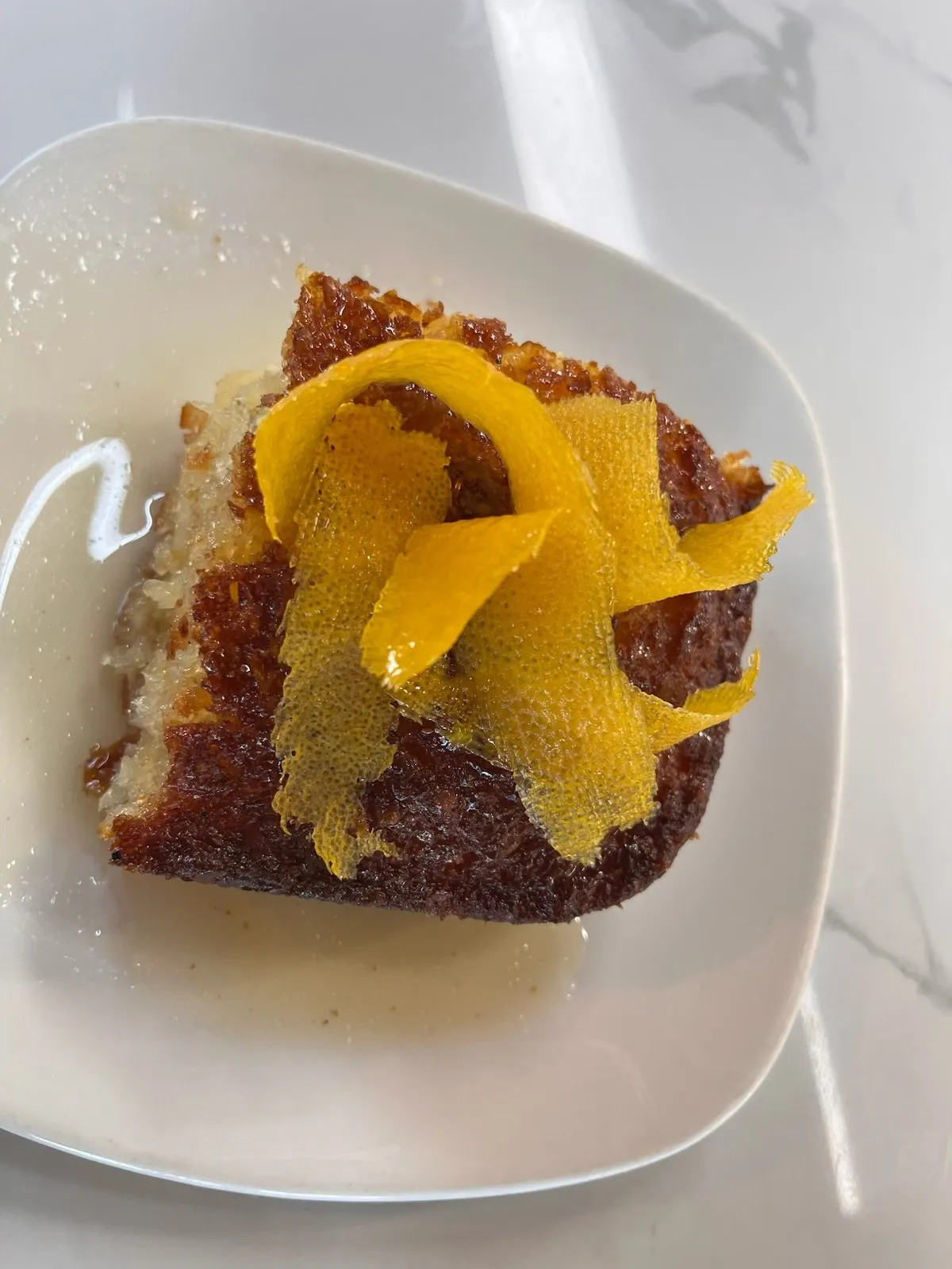 A square of portokalopita, Greek orange cake, topped with candied orange peel on a white plate